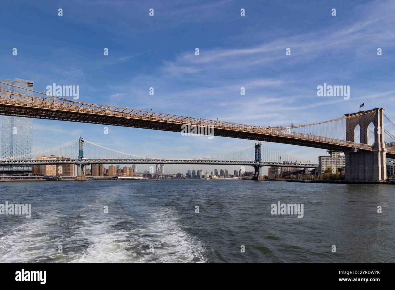 Eine atemberaubende Aussicht zeigt zwei markante Brücken, die den East River in New York City an einem klaren Tag von einer Fähre aus überqueren. Stockfoto