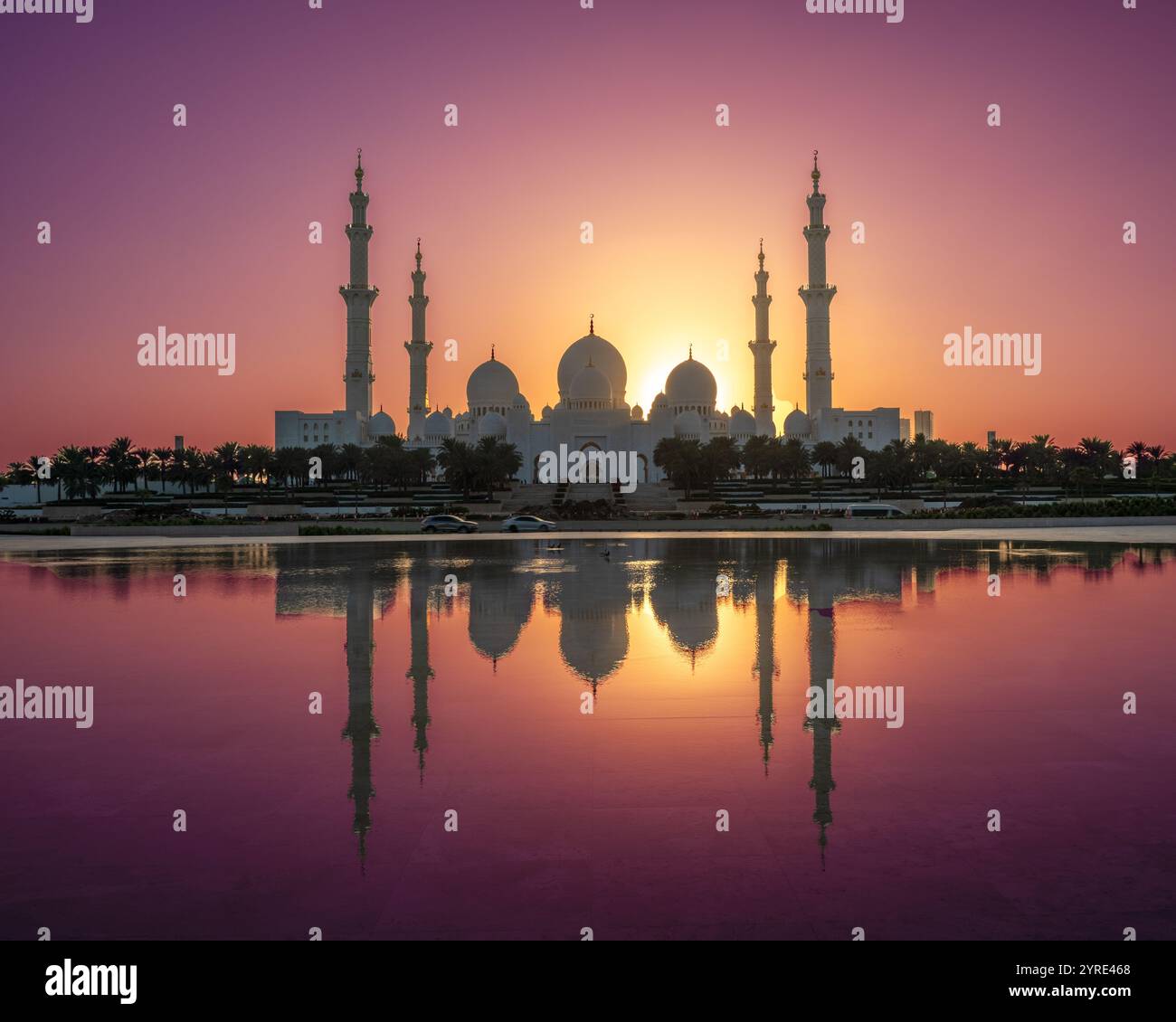 Scheich Zayed große Moschee bei Sonnenuntergang in Abu Dhabi mit einer atemberaubenden Reflexion auf dem Wasser. Leuchtende Lila-, Orange- und Gelbtöne beleuchten die Szene. Stockfoto