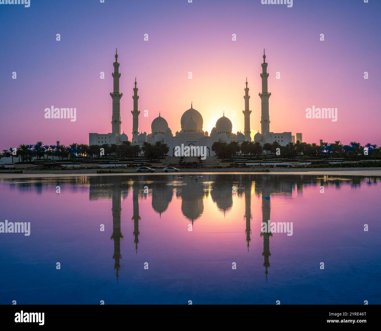 Scheich Zayed große Moschee bei Sonnenuntergang mit atemberaubenden Reflexionen im ruhigen Wasser und leuchtendem lila und orangen Himmel, Abu Dhabis Wahrzeichen Stockfoto