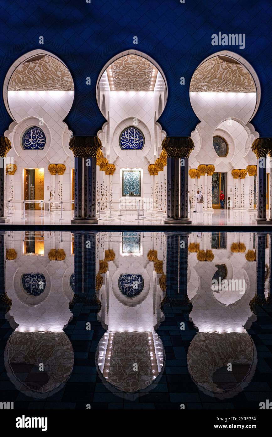 Beleuchtete Kolonnade der Scheich-Zayed-Moschee mit atemberaubenden Reflexionen im Innenhof Pool bei Nacht, Abu Dhabi, VAE. Stockfoto