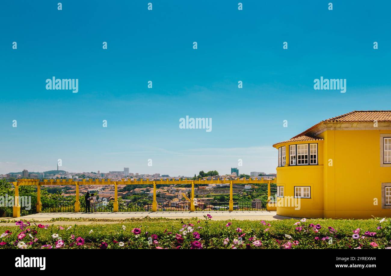 Panoramablick auf die Stadtlandschaft von porto mit einem lebhaften gelben Gebäude im Vordergrund, umgeben von bunten Blumen und einem klaren blauen Himmel im Garten Stockfoto