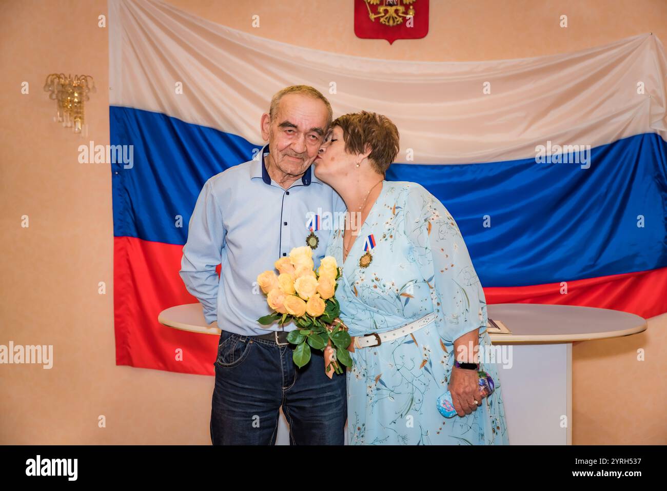 Ein russisches Paar feiert seinen goldenen Hochzeitstag im Standesamt. Das ältere Ehepaar, beide über 70 Jahre alt, trägt stolz Medaillen und teilt eine Stockfoto