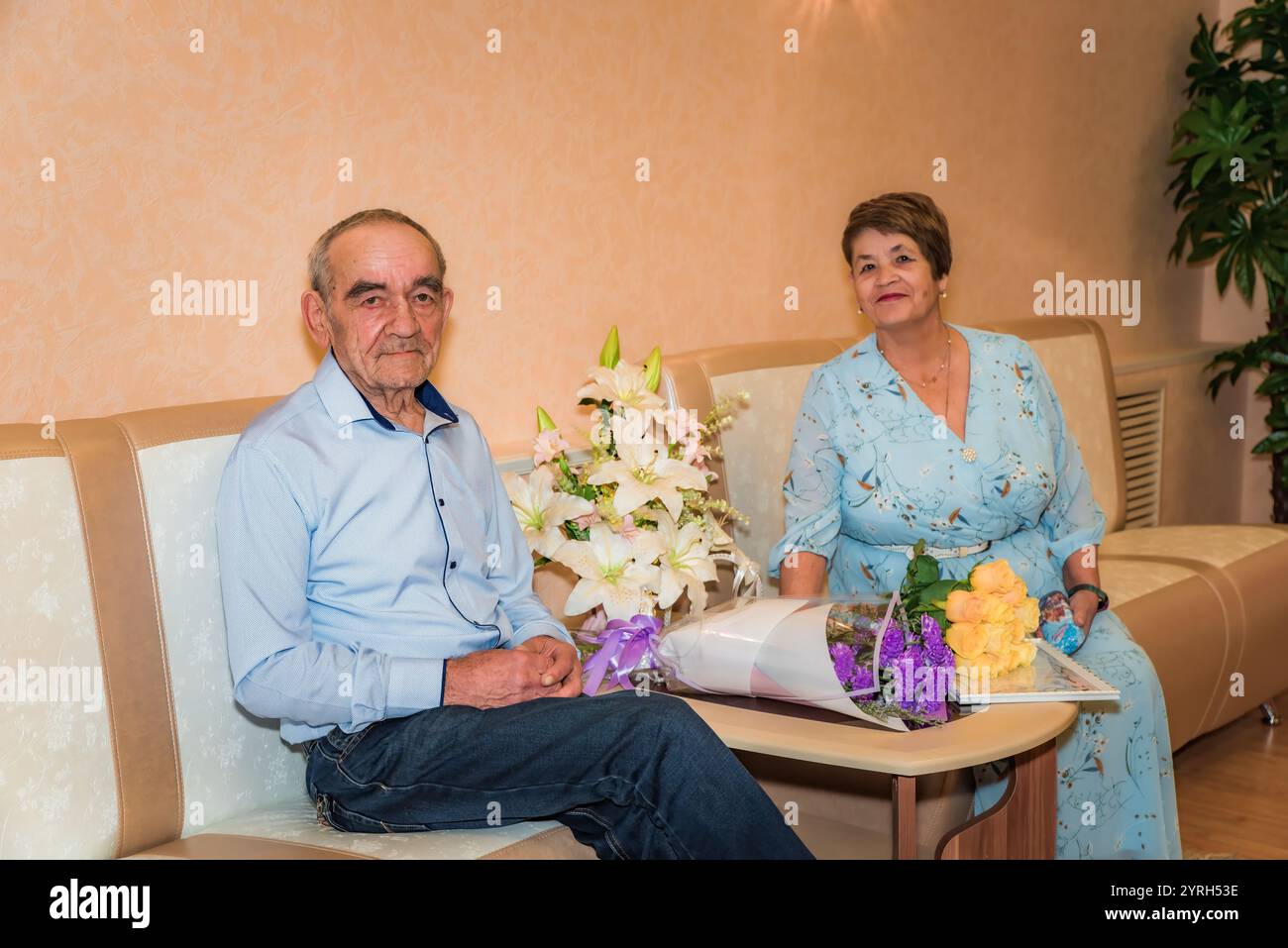 Das russische Paar über 70 feiert seine goldene Hochzeit im Standesamt. Sie sitzen in festlicher Kleidung auf Sofas, lächeln in die Kamera, mit Bouquen Stockfoto