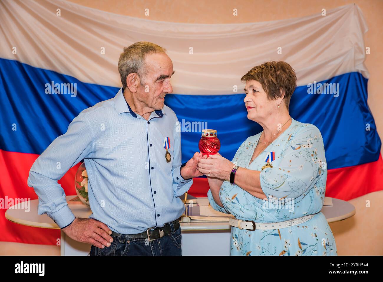 Der 76-jährige Mann und eine 71-jährige Frau feiern ihren goldenen Hochzeitstag (50 Jahre) in festlicher Kleidung und halten eine rote Lampe, die den Glauben symbolisiert Stockfoto