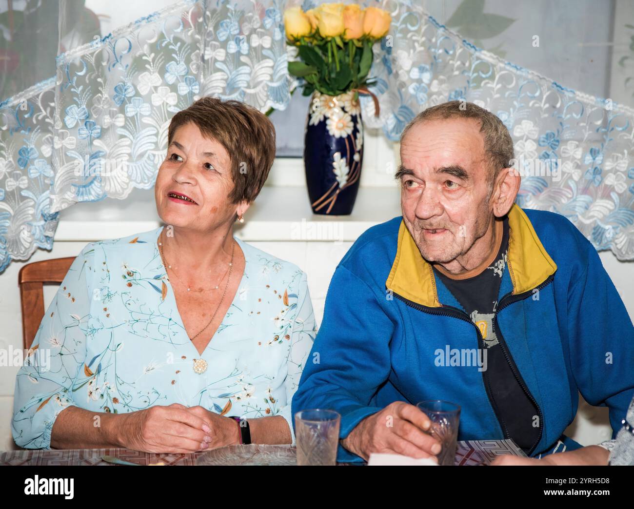 Ein russisches Paar, beide über 70 Jahre alt, schaut auf einen Fernseher. Sie sind festlich gekleidet, mit Brillen auf dem Feiertagstisch in t Stockfoto