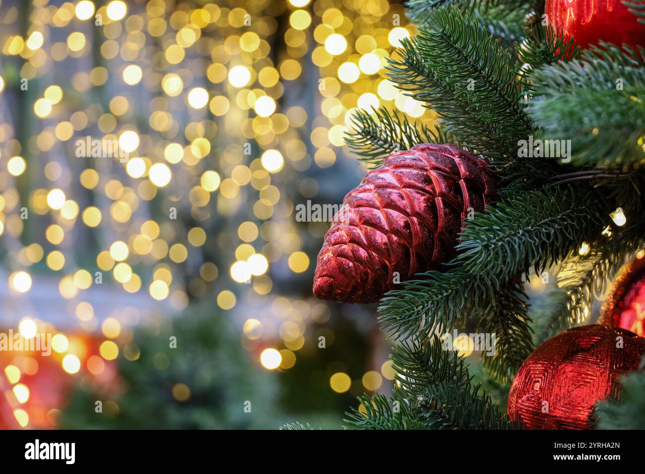 Neujahrsfeier, Weihnachtsbaumzweige mit Spielzeugkegel auf goldenem Lichterhintergrund Stockfoto