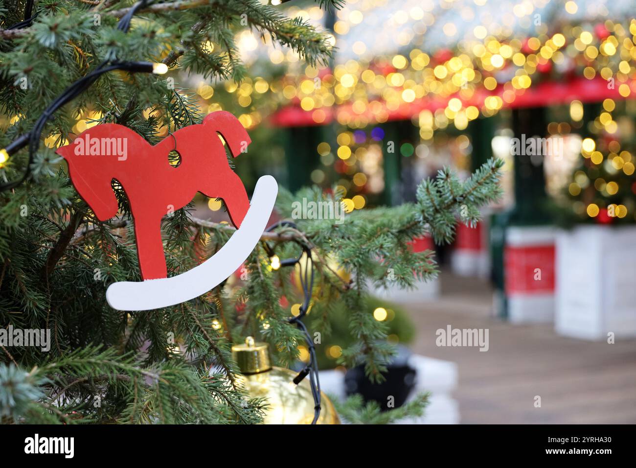 Neujahrsfeier, Weihnachtsbaumzweige mit Spielzeugpferd auf goldenem Lichterhintergrund Stockfoto