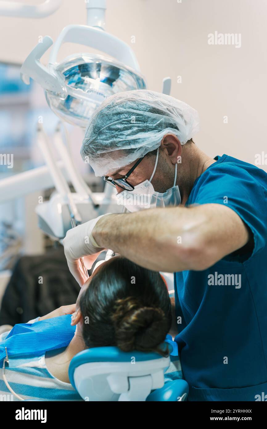 Ein Zahnarzt in blauen Peelings und Schutzausrüstung konzentriert sich auf die Behandlung eines Patienten in einem Zahnarztstuhl, umgeben von modernen Geräten in einem hellen Klinikset Stockfoto