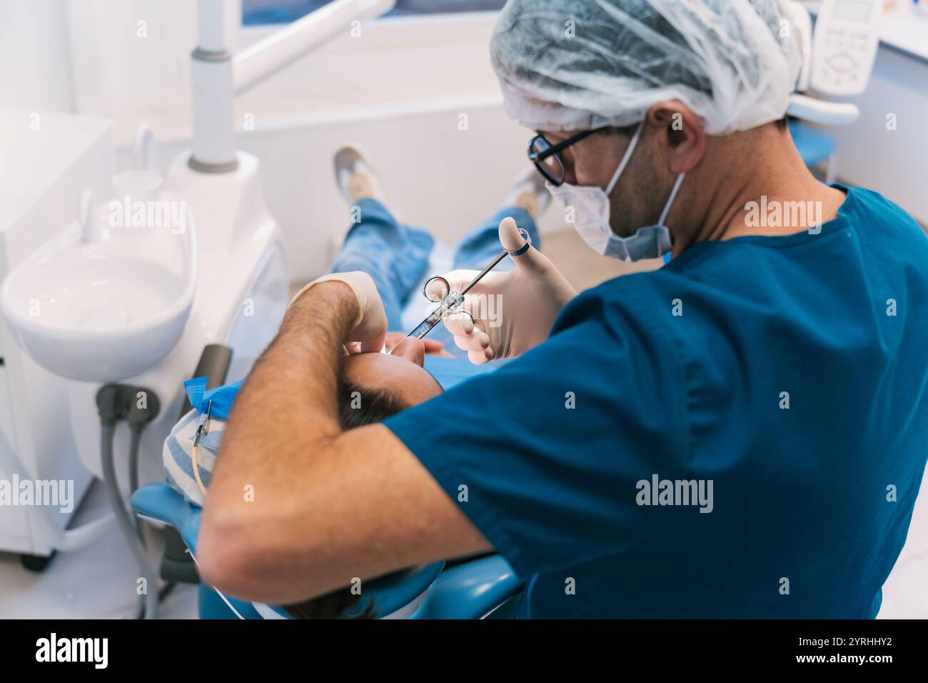 Der Zahnarzt in blauen Peelings und Maske betäubt einen Patienten auf einem Zahnarztstuhl. Klinisches Umfeld hebt Professionalität und Delle im Gesundheitswesen hervor Stockfoto