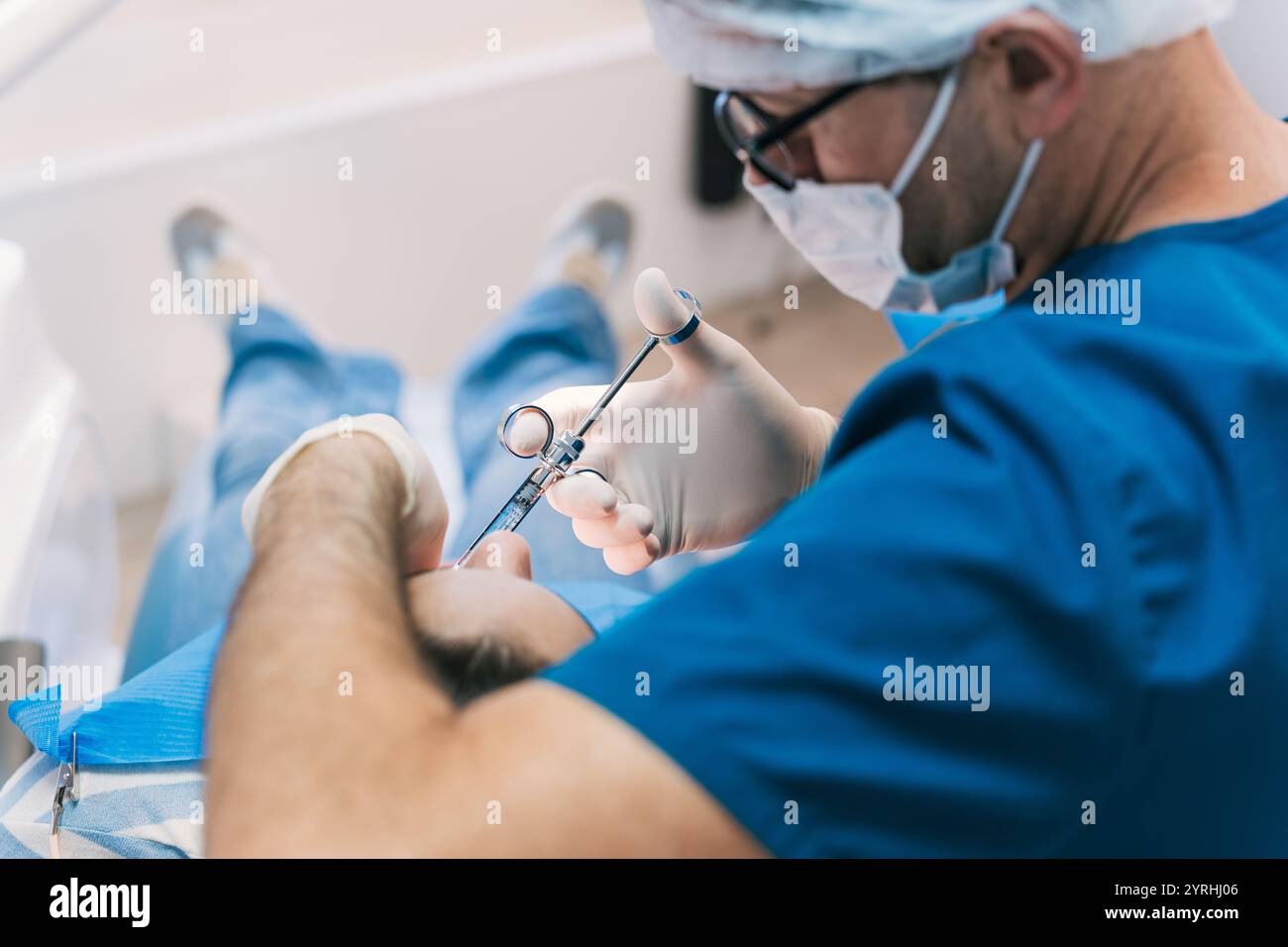 Ein Zahnarzt in blauen Peelings und Gesichtsmaske verabreicht einem Patienten sorgfältig Narkose. Der Schwerpunkt liegt auf Präzision und Pflege in einer Zahnklinik. Stockfoto