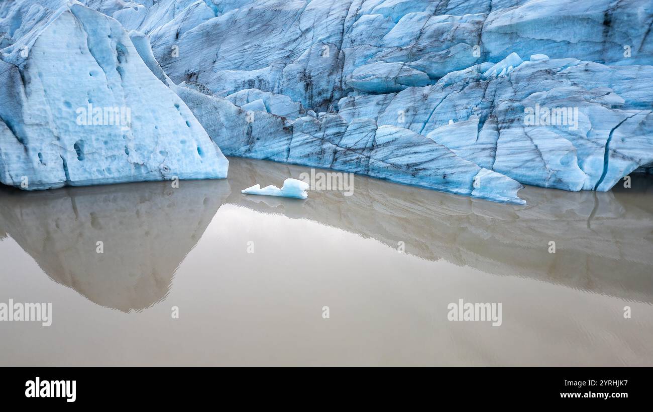 Blauer Gletscher mit einzigartigen Texturen spiegelt sich in einem ruhigen Wasserkörper wider. Die ruhige Landschaft unterstreicht die natürliche Schönheit und die komplizierten Details des Gletschers Stockfoto