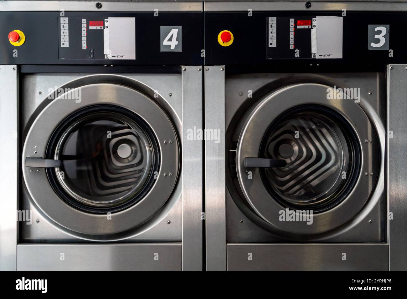 Nahaufnahme von zwei großen industriellen Waschmaschinen in einer modernen Waschanlage mit Edelstahldesigns und digitalen Bedienfeldern. Stockfoto