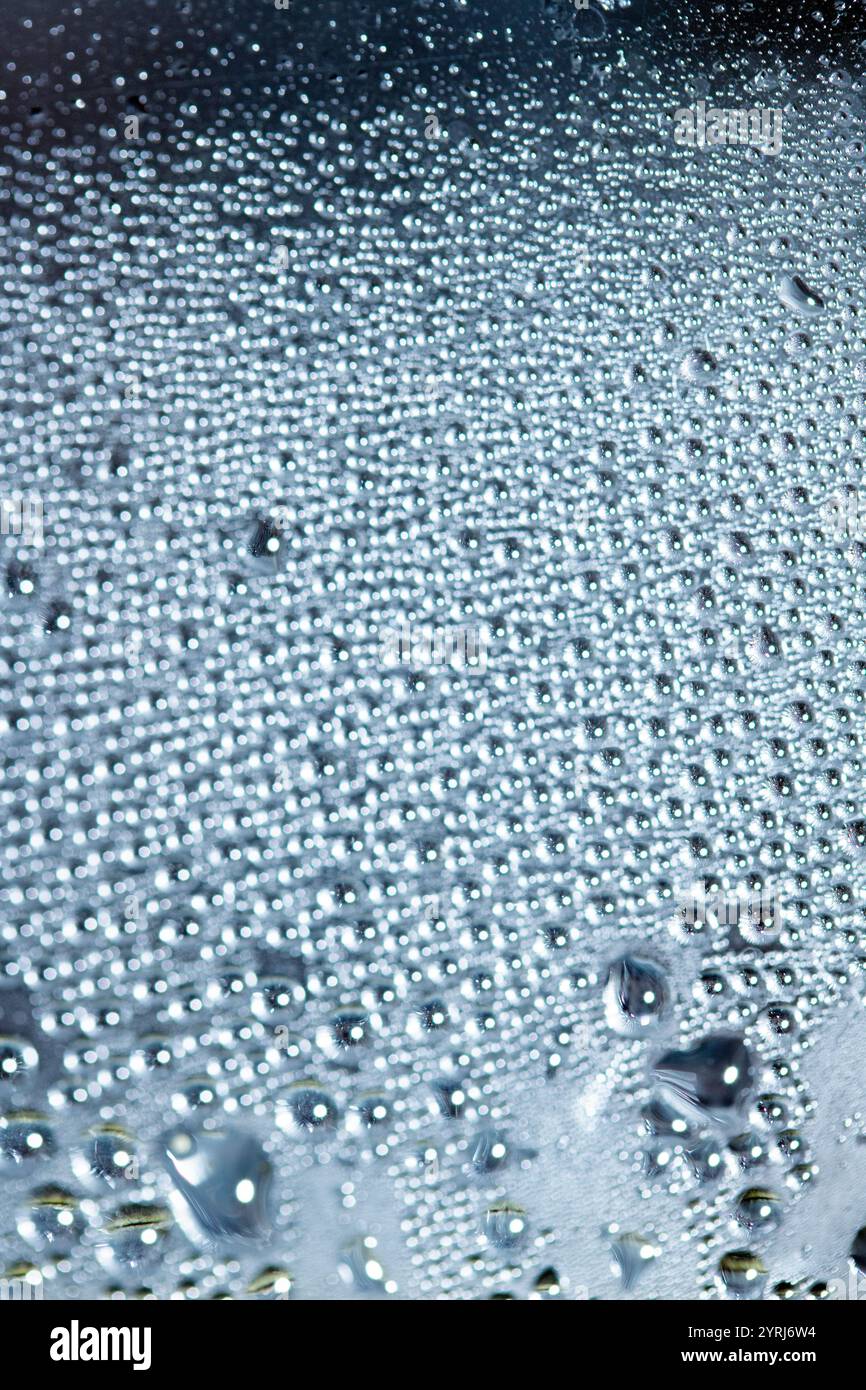 Blaue Regen-Blasen fallen auf einem feuchten Tag ein Fenster hinunter. Abstrakter Hintergrund Stockfoto