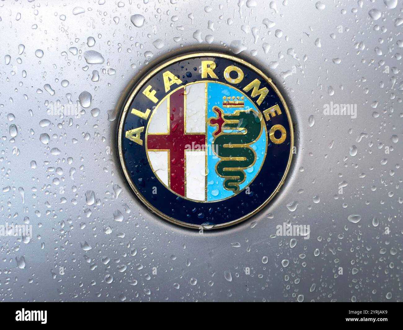 Nahaufnahme eines Logos auf der A1999 Alfa Romeo 166 V6 Motorhaube mit Wassertropfen - Smartphone-aufgenommenes Stockfoto