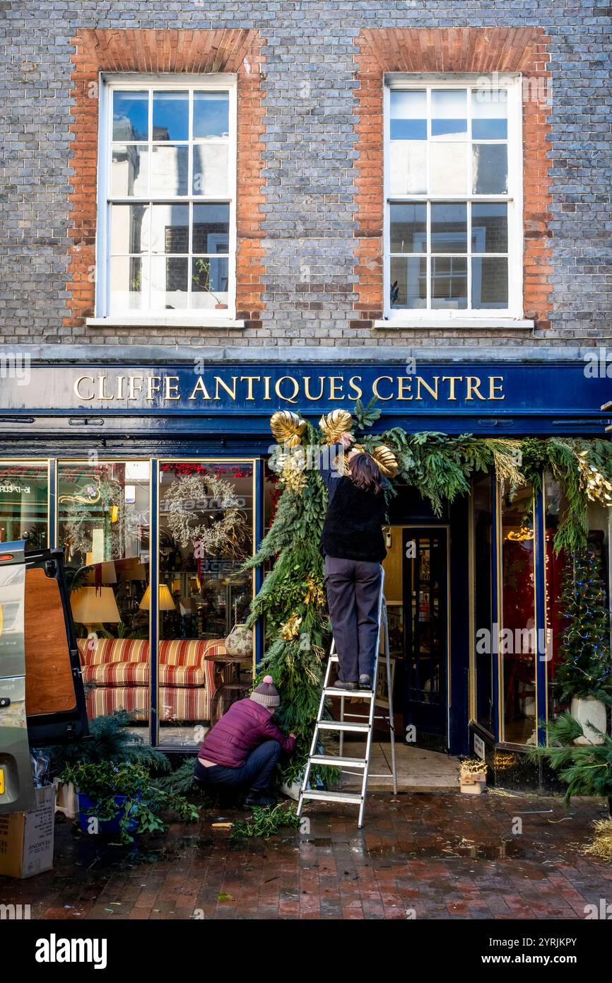 Leute, die Weihnachtsdekorationen vor einem Antiquitätenladen in der High Street, Lewes, East Sussex, Großbritannien aufhängen. Stockfoto