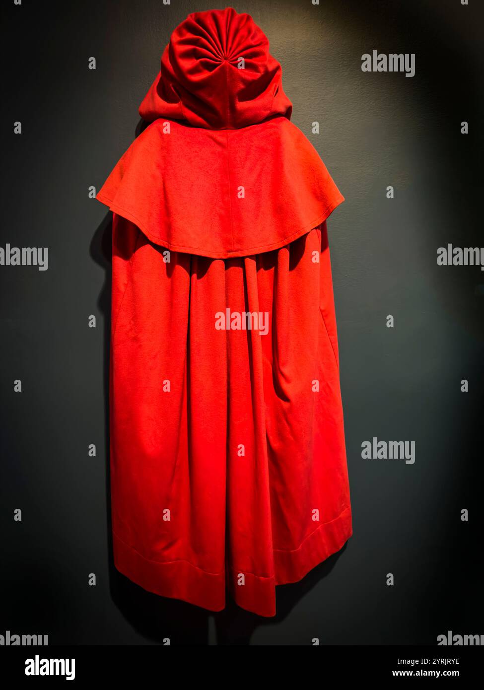 Leuchtend roter Mantel mit Kapuze vor dunklem Hintergrund, der den reichhaltigen Stoff unterstreicht – wie die Kleidung in der Geschichte einer Magd Stockfoto