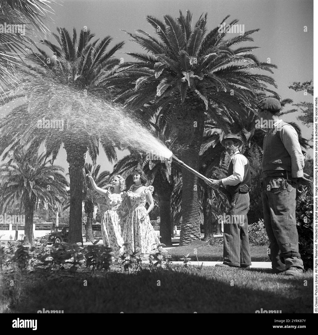 Die Schauspielerinnen in Lissabon, Portugal, 1949. Gaby Stenberg (1923–2011) mit Margareta Fahlén (1918–1978) die beiden Schauspielerinnen sind in Portugal, im Badeort Estoril außerhalb von Lissabon, um in dem Film VI Flyger på Rio zu erscheinen. Im Garten des Hotels, während ein Mann gesehen wird, wie er die Pflanzen und Bäume tränkt. Kristoffersson Ref. AR84-5 *** Lokaler Titel *** Stockfoto