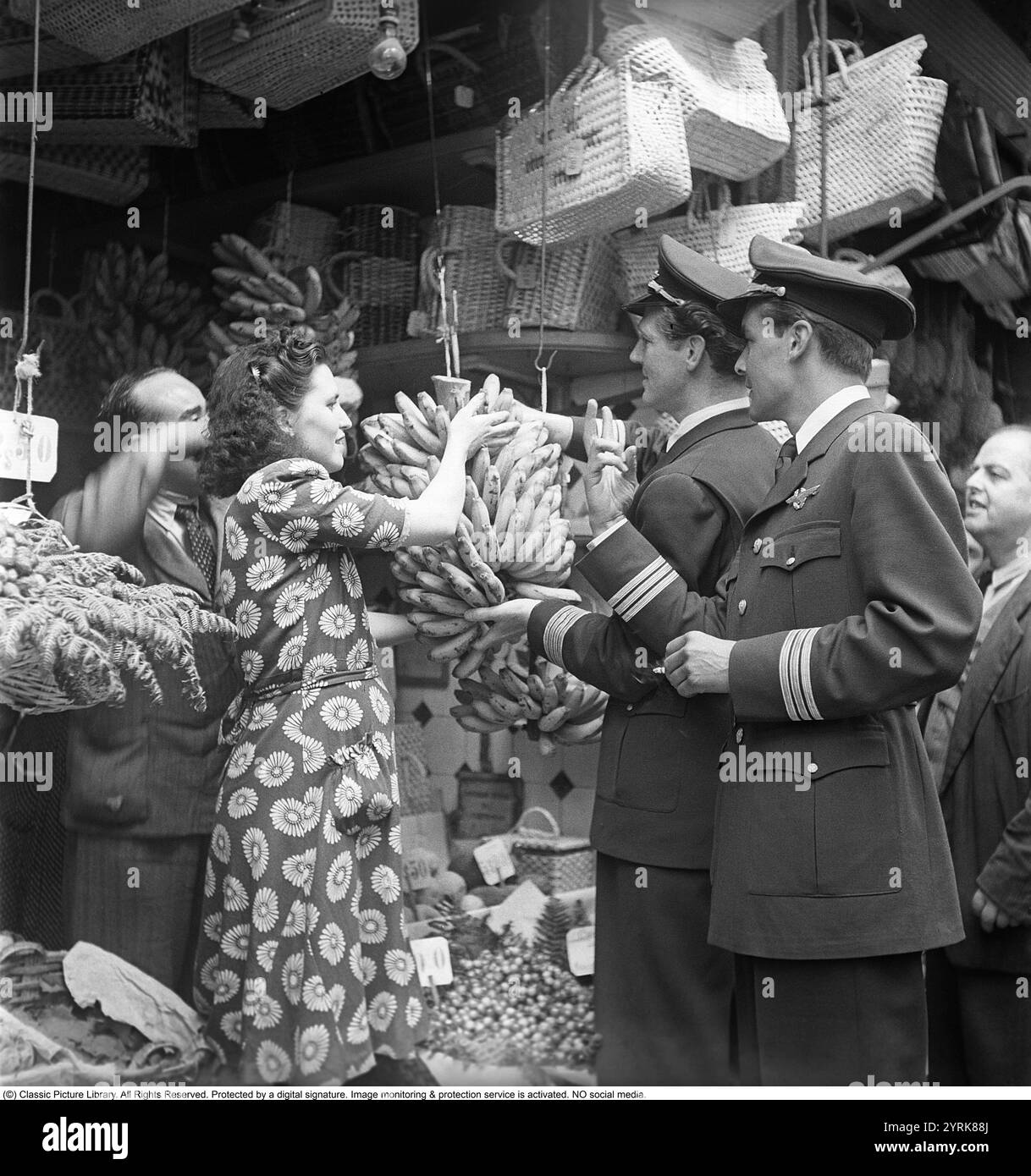 Lissabon, Portugal, 1949. Zwei schwedische Flugkapitän in ihren Uniformen kaufen Bananen in einem Geschäft, das von einem Mädchen des Ladenpersonals unterstützt wird. Kristoffersson Ref. AR87-5 *** Lokaler Titel *** Stockfoto
