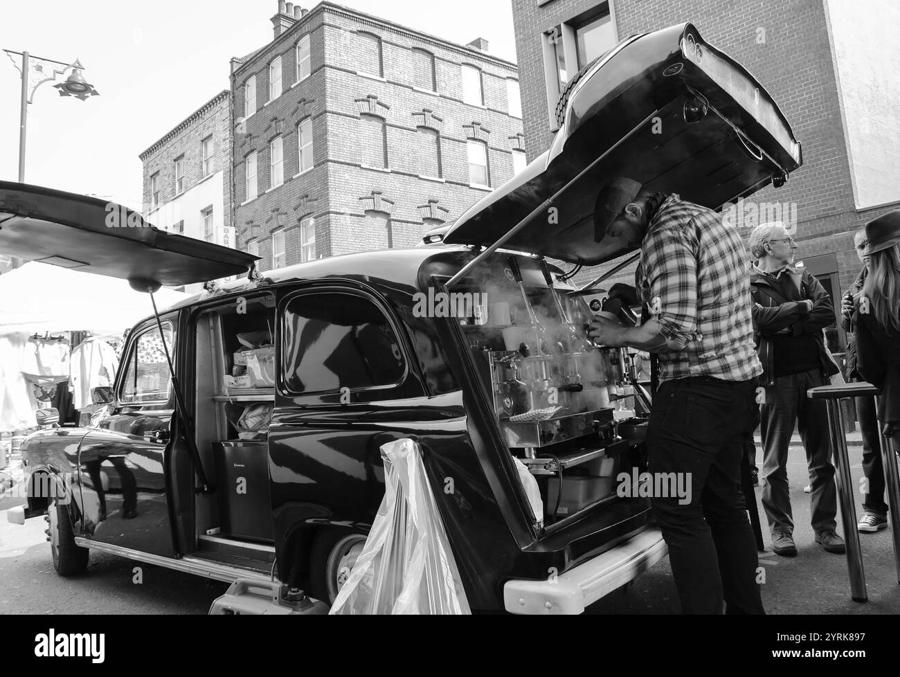 LONDON, ENGLAND, Großbritannien - 4. MAI 2014: Barista kocht Kaffee im mobilen Café (ehemaliges altes Taxi) im Brick Lane Market Area. Schwarzweißes historisches Foto. Stockfoto
