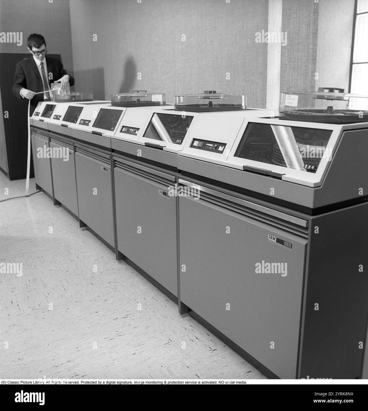 IBM-Mainframe-System 360. Ein Mann in einem Raum, in dem Computergeräte sichtbar sind. Die IBM 2311 Direct Access Storage Facility wurde 1964 für den Einsatz in der gesamten System/360-Computerfamilie eingeführt. Es hat bis zu 7,25 MB auf einem einzigen Wechseldatenträger-Pack gespeichert. Der 2311 wurde mit einer IBM-Standardschnittstelle geliefert, was zu einer ganzen Branche von „Plug-kompatiblen“ Festplattenherstellern wie Control Data Corporation und Memorex führte. Kristoffersson Ref. DY127-2 Stockfoto