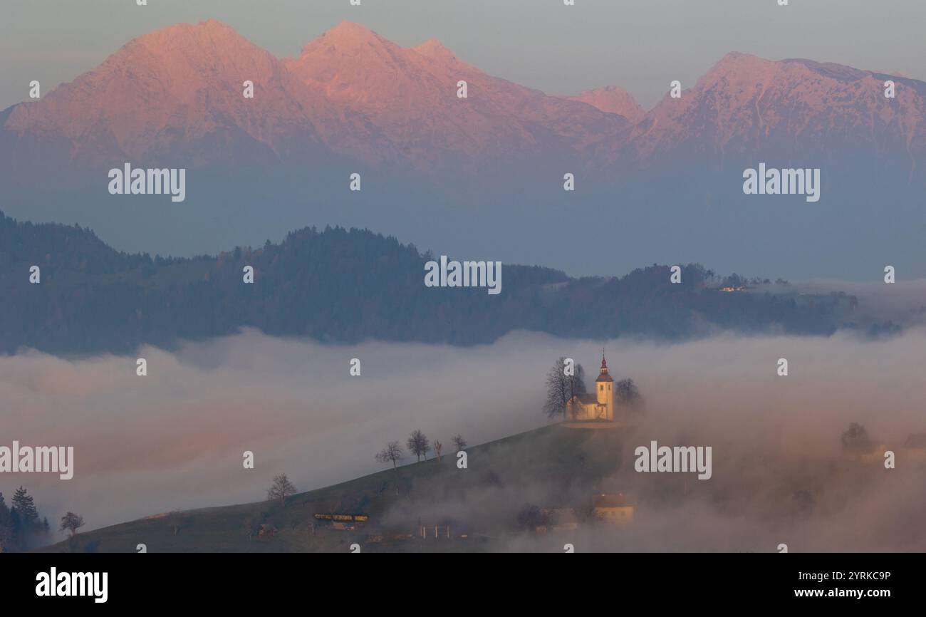 Landschaft der slowenischen Alpen mit St. Primoz Kirche, Wahrzeichen umgeben von dichtem Nebel Stockfoto