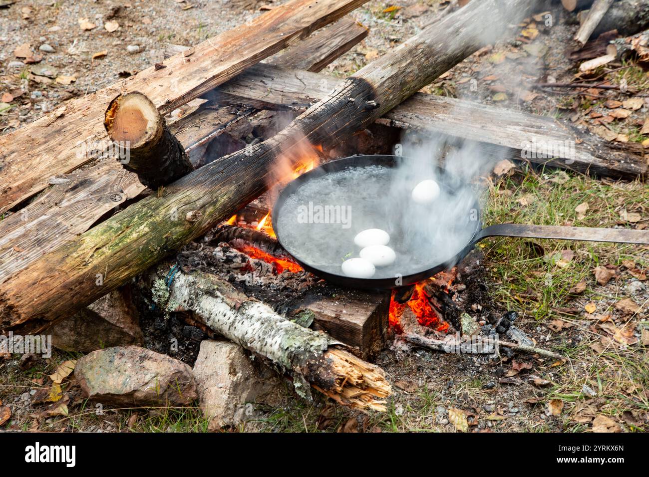 Nahaufnahme eines rot heißen, knisternden Holzfeuers im Freien mit einer Pfanne gefüllt mit kochendem Wasser, in der Eier als Teil der Selbstversorgung gekocht werden o Stockfoto
