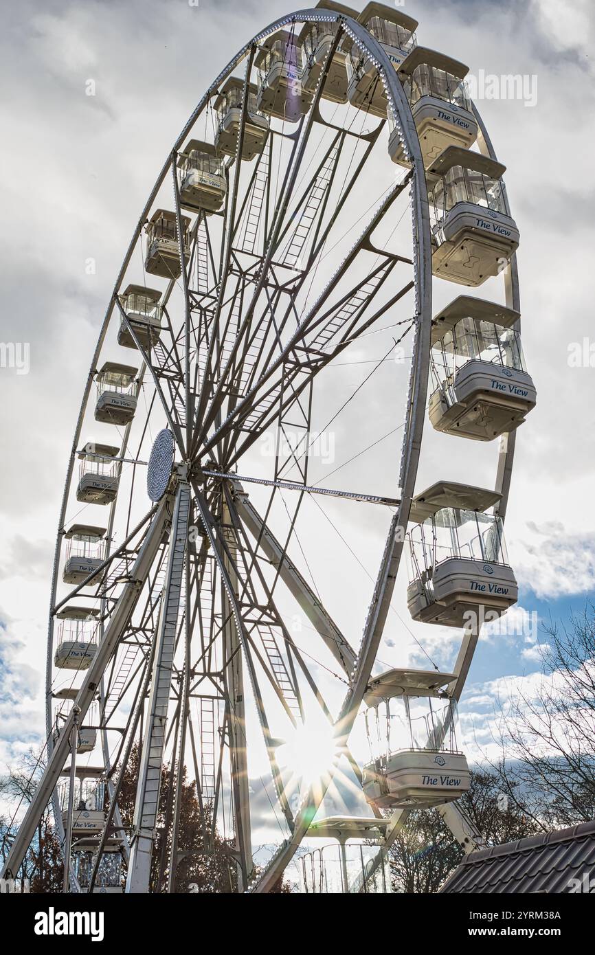 Ein flacher Blick auf ein Riesenrad, „The View“, vor einem bewölkten Himmel. Die Sonne scheint durch die Speichen des Rades und beleuchtet die Fahrgastgondeln. Stockfoto