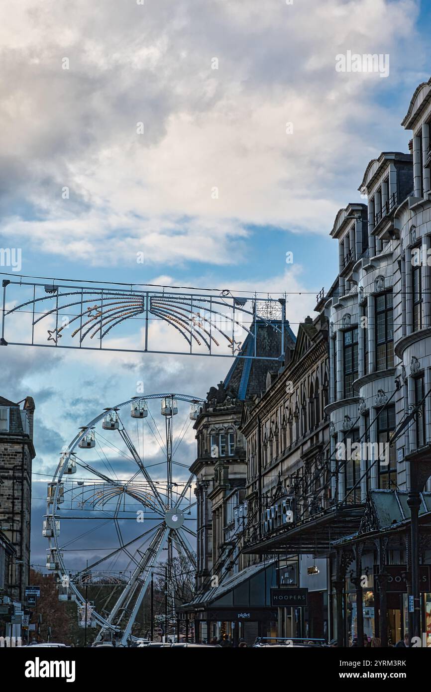 Ein Riesenrad ist zwischen Gebäuden zu sehen, die mit Weihnachtslichtern vor einem bewölkten Himmel geschmückt sind. Die Architektur besteht hauptsächlich aus Stein, mit verzierten Deta Stockfoto
