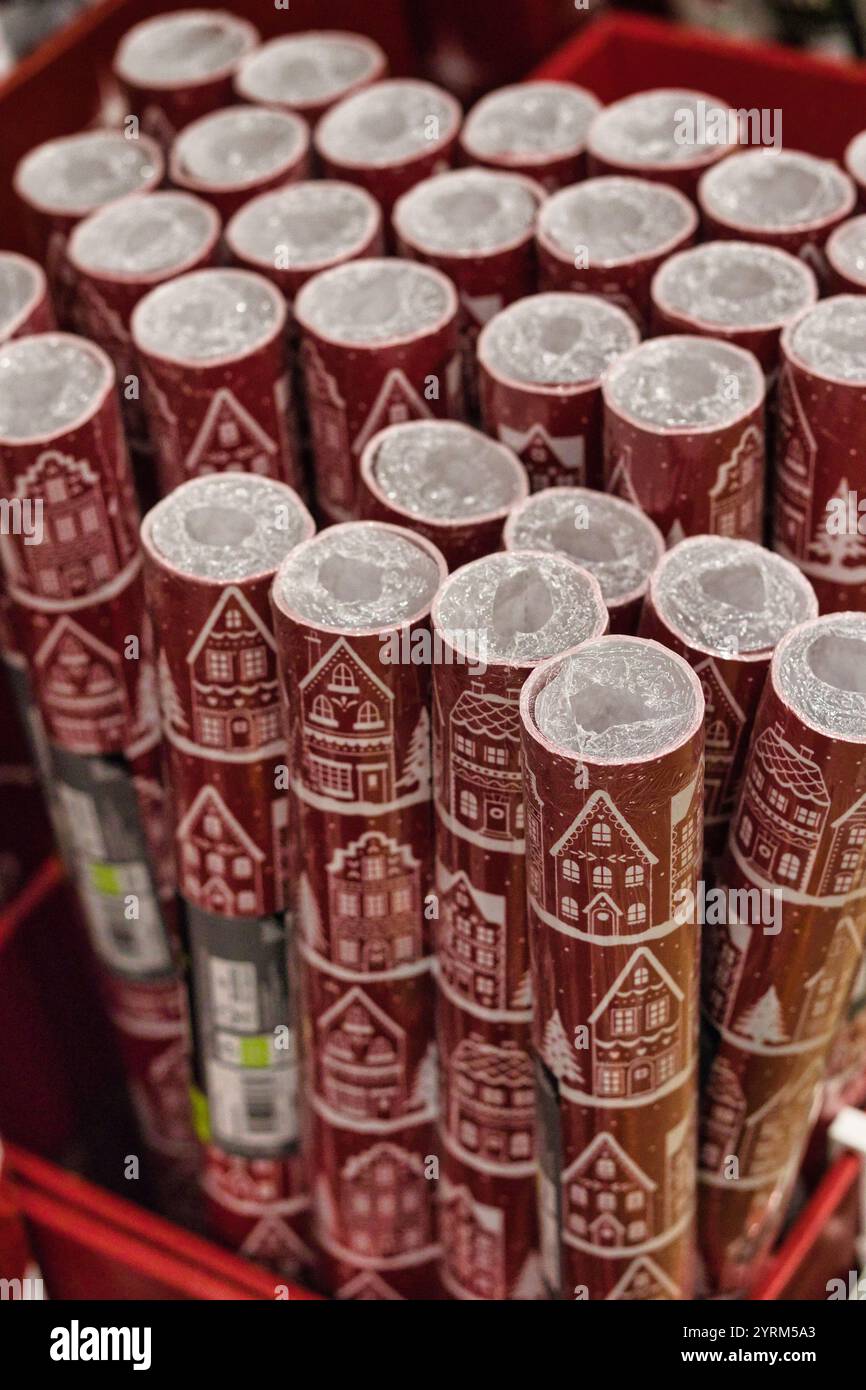 Zahlreiche Rollen rotes Geschenkpapier mit weißem Lebkuchenhausmuster sind in einem roten Behälter eng angeordnet. Die Kunststoffverpackung auf der Rolle Stockfoto