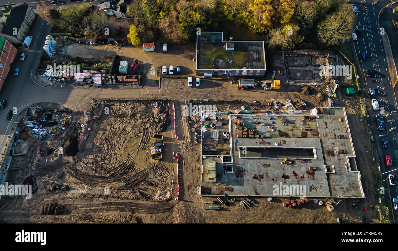 Luftaufnahme einer Baustelle mit ausgehobener Erde, teilweise gebauter Betonplatte, Baumaterialien und angrenzendem Bestand Stockfoto