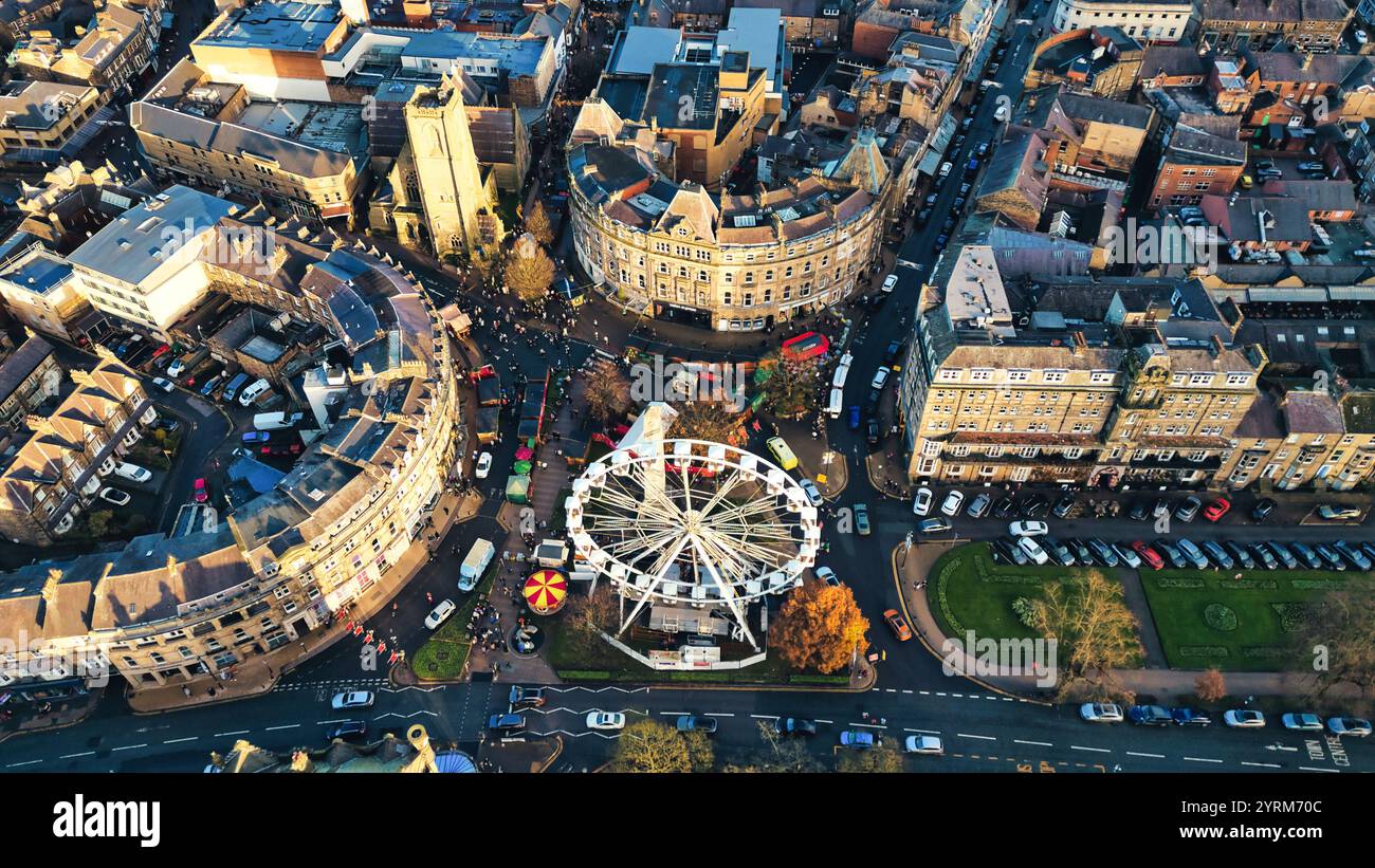 Blick aus der Vogelperspektive auf einen Stadtplatz mit Riesenrad, umgeben von Gebäuden, geparkten Autos und Fußgängern. Die Gebäude sind hauptsächlich mehrstöckig und ston Stockfoto