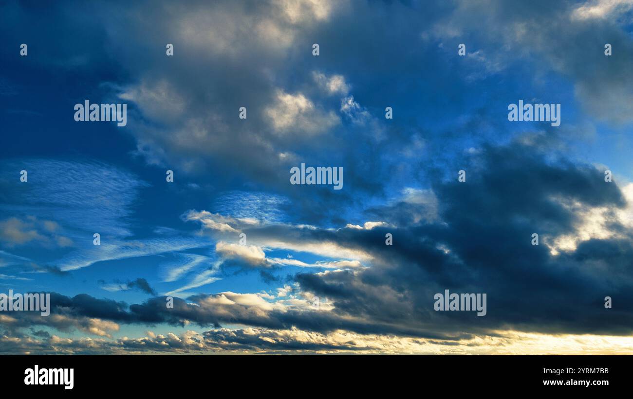 Eine weite Aufnahme eines meist bewölkten Himmels. Der Himmel zeigt eine Mischung aus dunklen, grau-blauen Wolken und helleren, weißen und grauen Cumulus-Wolken. Blaue Flecken Stockfoto