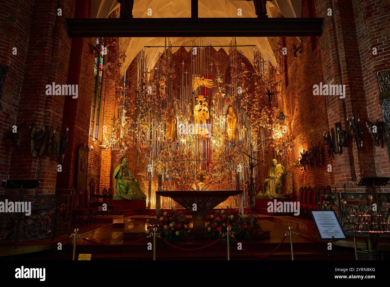 Ein kunstvoll verziertes Innere einer Danziger Kirche mit einem atemberaubenden Altar, der mit goldenen Bernsteinskulpturen, Blumendekorationen und Statuen geschmückt ist, beleuchtet von Stockfoto