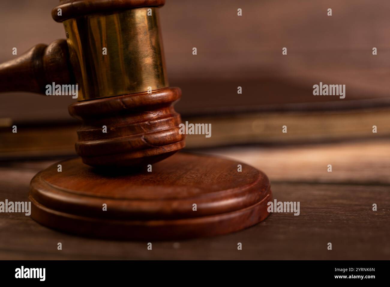 Hölzerner Hammer auf Tonblock, legales Buch verschwimmt im Hintergrund. Symbol für Gerechtigkeit, Recht, Auktion und Gericht. Stockfoto