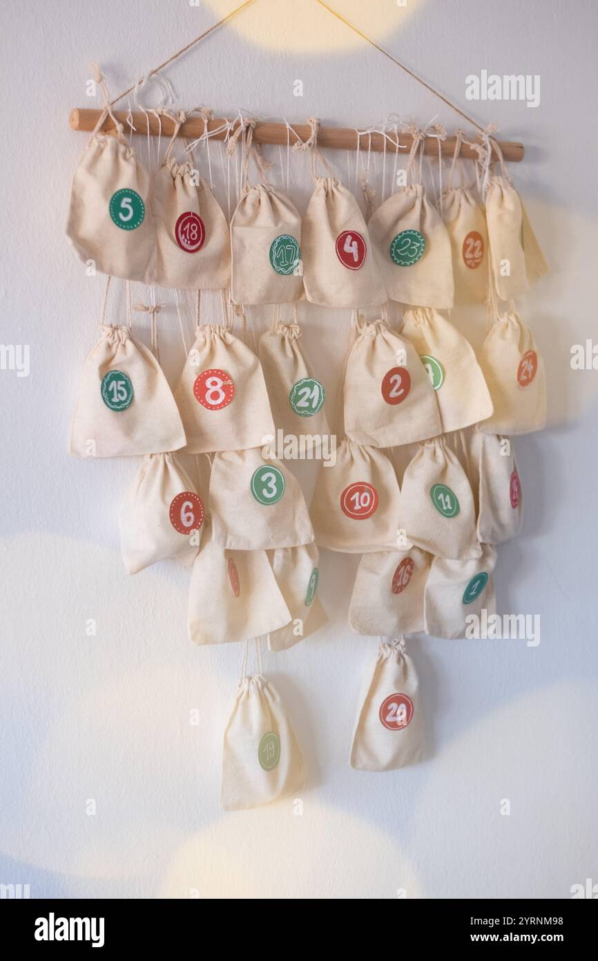 DIY Adventskalender mit Stofftüten, die an einer Holzstange hängen und mit den Zahlen 1 bis 24 an den Taschen hängen. Stockfoto