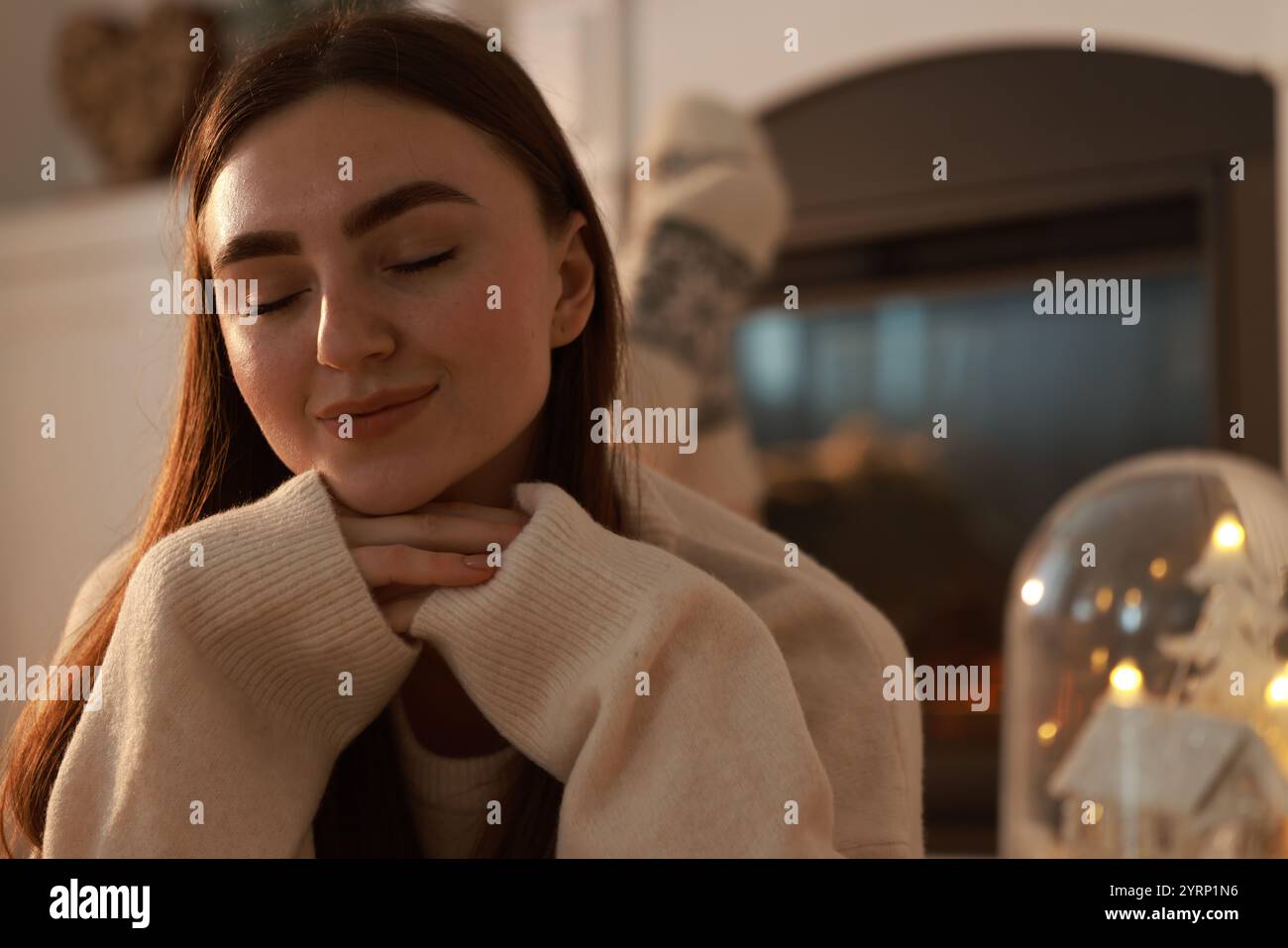 Frau in warmem Pullover, die zu Hause neben dem Kamin ruht Stockfoto
