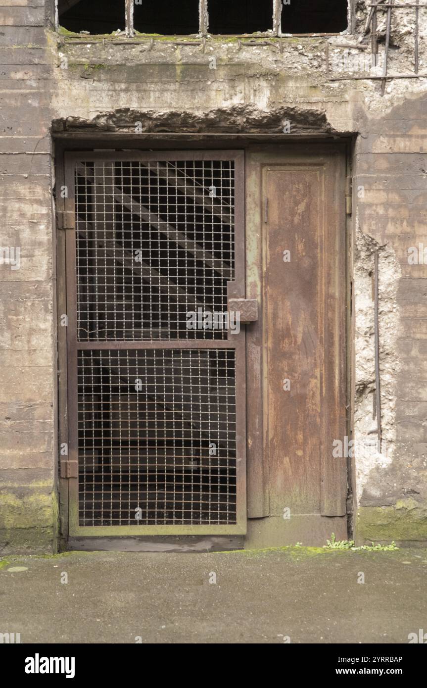 Alte, rostige Metalltür mit Gitter, die den Zugang zum verlassenen Industriegebäude blockiert Stockfoto