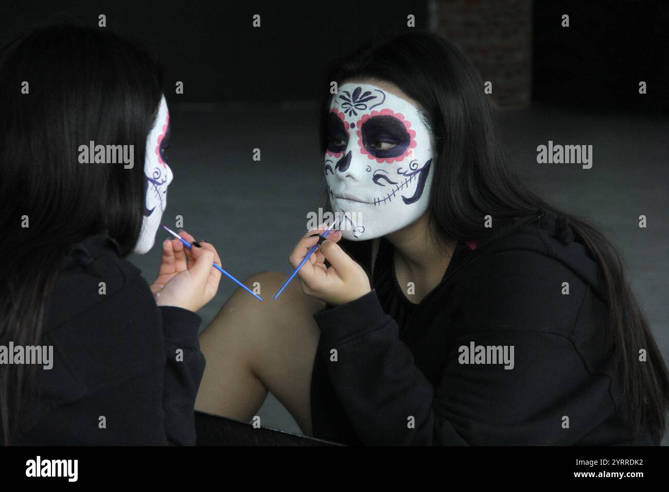 Die junge Mexikanerin schminkt catrina vor dem Spiegel, um den Tag der Toten in Mexiko zu feiern Stockfoto