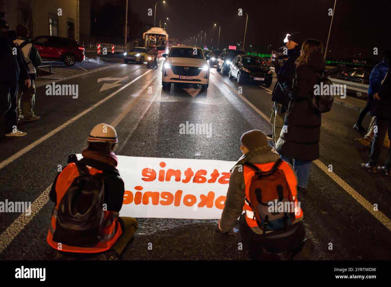 Demonstranten der Organisation der letzten Generation, die ein Banner halten, blockieren die Straße während einer Demonstration gegen den polnischen Premierminister Donald Tusks Klimapolitik. Aktivisten der Klimabewegung der letzten Generation (Ostatnie Pokolenie) haben seit vergangener Woche eine lang andauernde Kampagne zur Blockierung wichtiger Routen während der Hauptverkehrszeiten gestartet, wobei sich einige Demonstranten an die Straßen kleben. Sie fordern, dass alle Mittel für neue Schnellstraßen- und Autobahnprojekte stattdessen auf die Verbesserung des öffentlichen Verkehrs ausgerichtet werden und dass billige Monatskarten für die Nutzung des öffentlichen Verkehrs eingeführt werden Stockfoto
