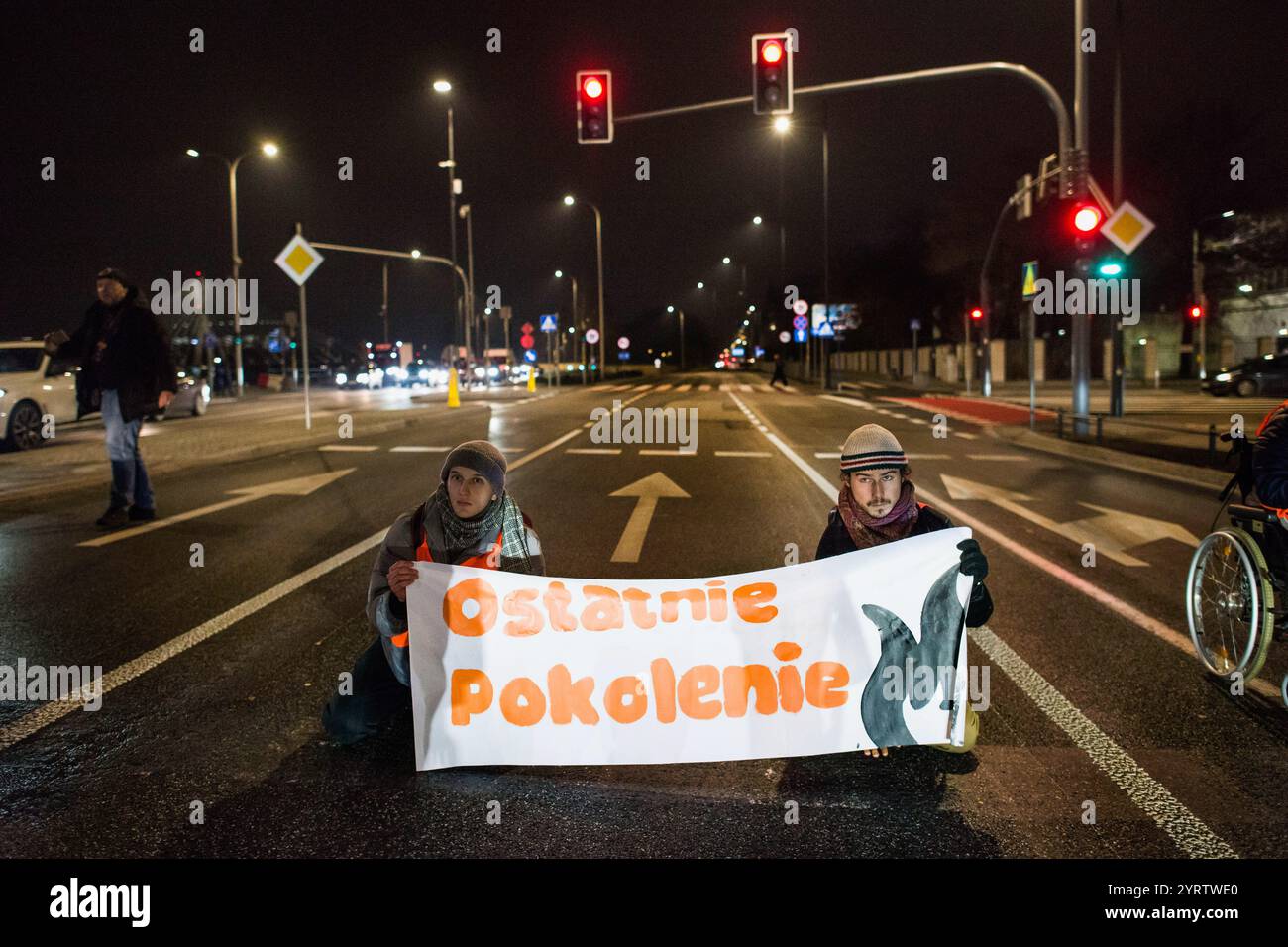 Demonstranten der Organisation der letzten Generation, die ein Banner halten, blockieren die Straße während einer Demonstration gegen den polnischen Premierminister Donald Tusks Klimapolitik. Aktivisten der Klimabewegung der letzten Generation (Ostatnie Pokolenie) haben seit vergangener Woche eine lang andauernde Kampagne zur Blockierung wichtiger Routen während der Hauptverkehrszeiten gestartet, wobei sich einige Demonstranten an die Straßen kleben. Sie fordern, dass alle Mittel für neue Schnellstraßen- und Autobahnprojekte stattdessen auf die Verbesserung des öffentlichen Verkehrs ausgerichtet werden und dass billige Monatskarten für die Nutzung des öffentlichen Verkehrs eingeführt werden Stockfoto