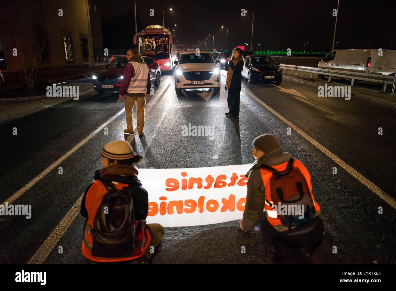 Demonstranten der Organisation der letzten Generation, die ein Banner halten, blockieren die Straße während einer Demonstration gegen den polnischen Premierminister Donald Tusks Klimapolitik. Aktivisten der Klimabewegung der letzten Generation (Ostatnie Pokolenie) haben seit vergangener Woche eine lang andauernde Kampagne zur Blockierung wichtiger Routen während der Hauptverkehrszeiten gestartet, wobei sich einige Demonstranten an die Straßen kleben. Sie fordern, dass alle Mittel für neue Schnellstraßen- und Autobahnprojekte stattdessen auf die Verbesserung des öffentlichen Verkehrs ausgerichtet werden und dass billige Monatskarten für die Nutzung des öffentlichen Verkehrs eingeführt werden Stockfoto