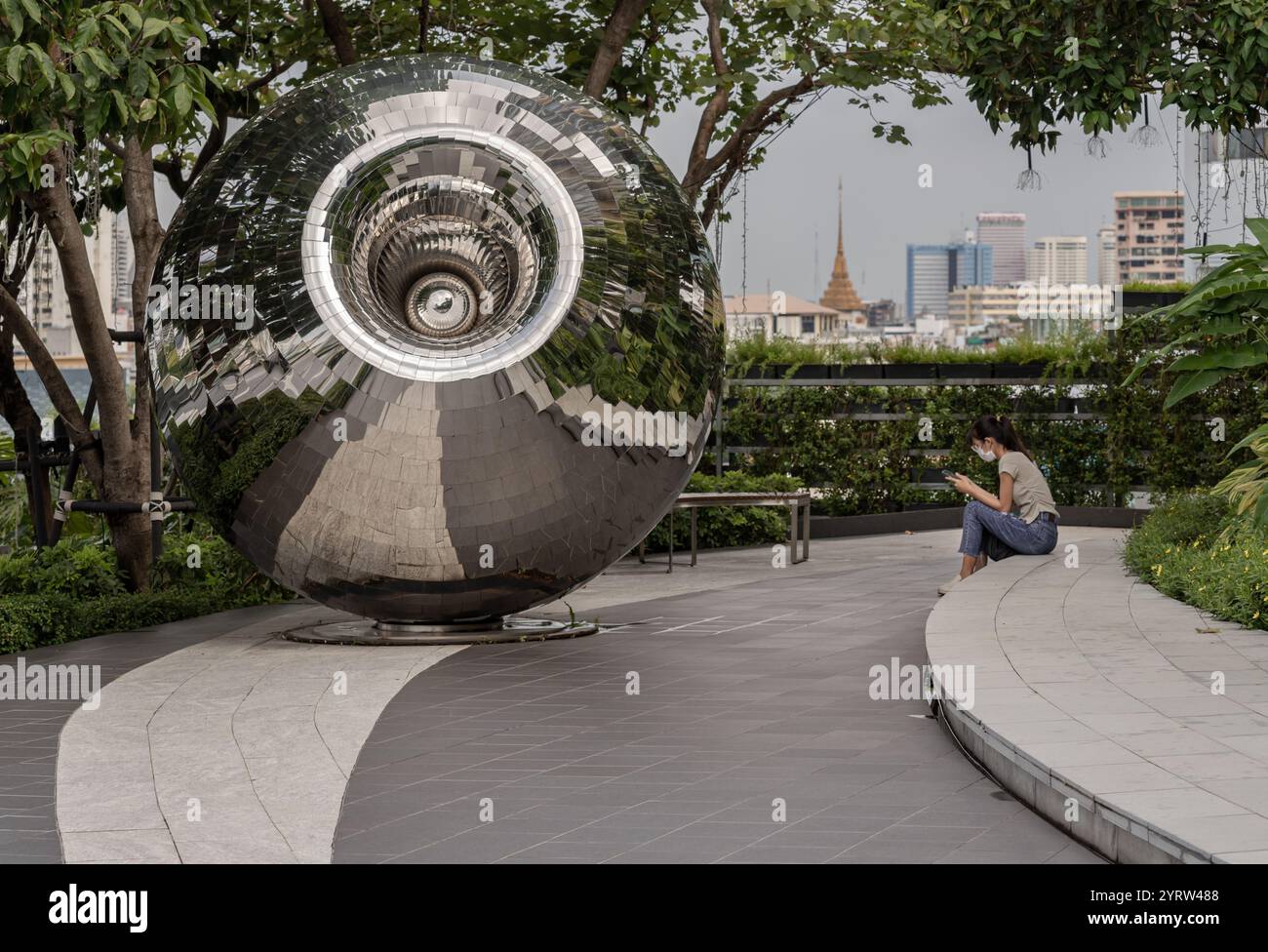 Bangkok, Thailand - 28. September 2024 - eine unbekannte junge Frau, die ein eifarbiges T-Shirt mit Jeans und Schutzmaske trägt und ein Smartphone benutzt Stockfoto