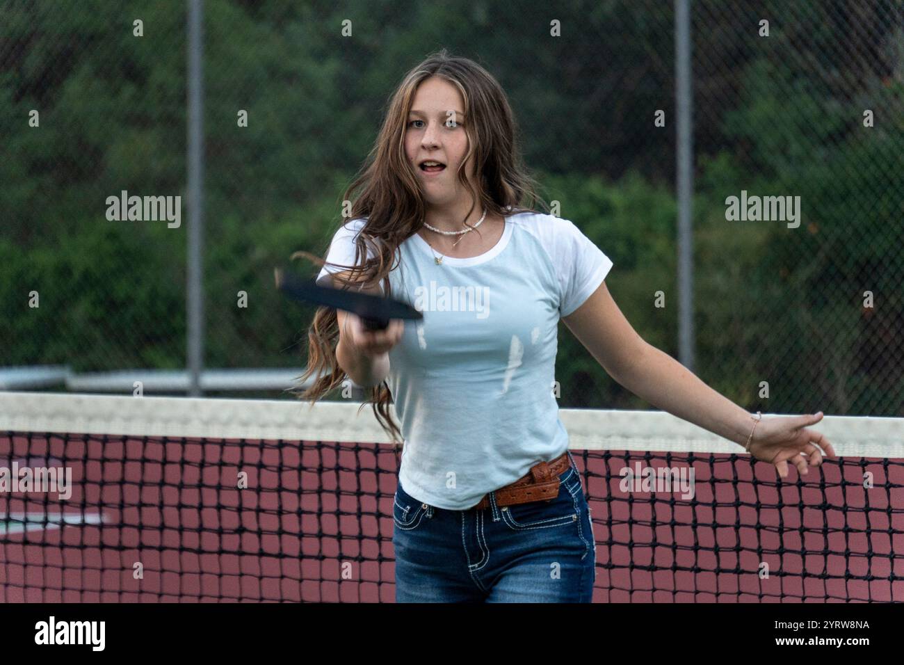 Das junge Mädchen genießt bei Abendlicht ein Tennisspiel auf dem Außenplatz Stockfoto