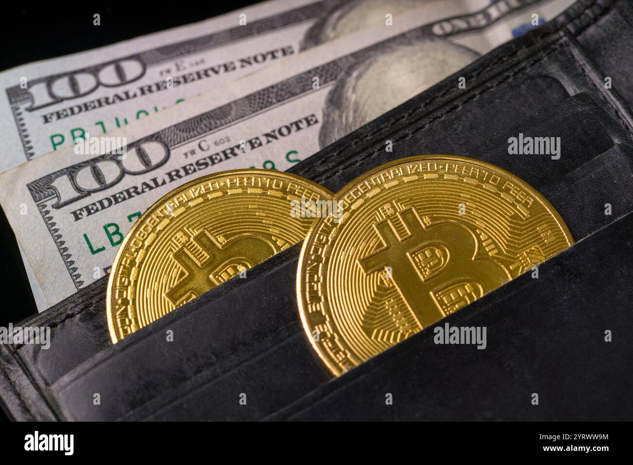 Bitcoin und 100 Dollar sichtbar in einer offenen schwarzen Ledergeldbörse Stockfoto