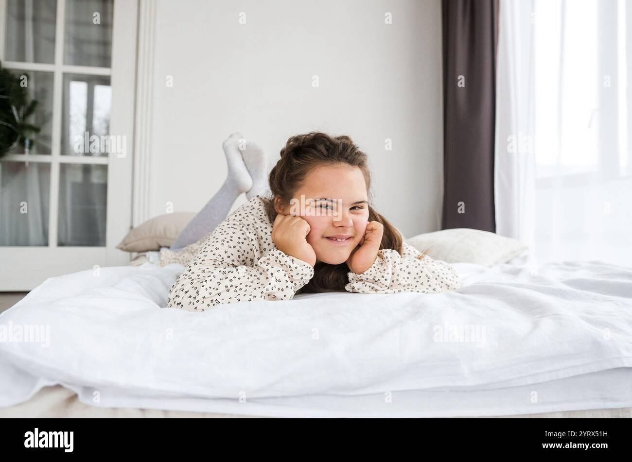 Eine junge Frau mit Down-Syndrom liegt glücklich auf einem Bett und lächelt zufrieden. Ihre entspannte Pose und ihr fröhlicher Ausdruck unterstreichen ihr Wohlbefinden und ihr Selbstbewusstsein. Stockfoto