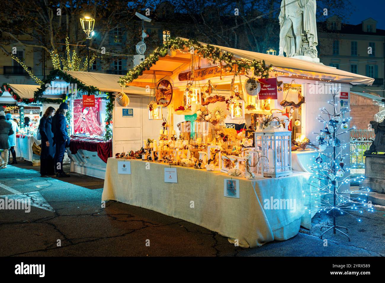 Ein lebhafter Weihnachtsmarkt, der abends beleuchtet wird und handgefertigtes Kunsthandwerk und leuchtende Laternen in der Stadt Asti, Italien, zeigt. Stockfoto