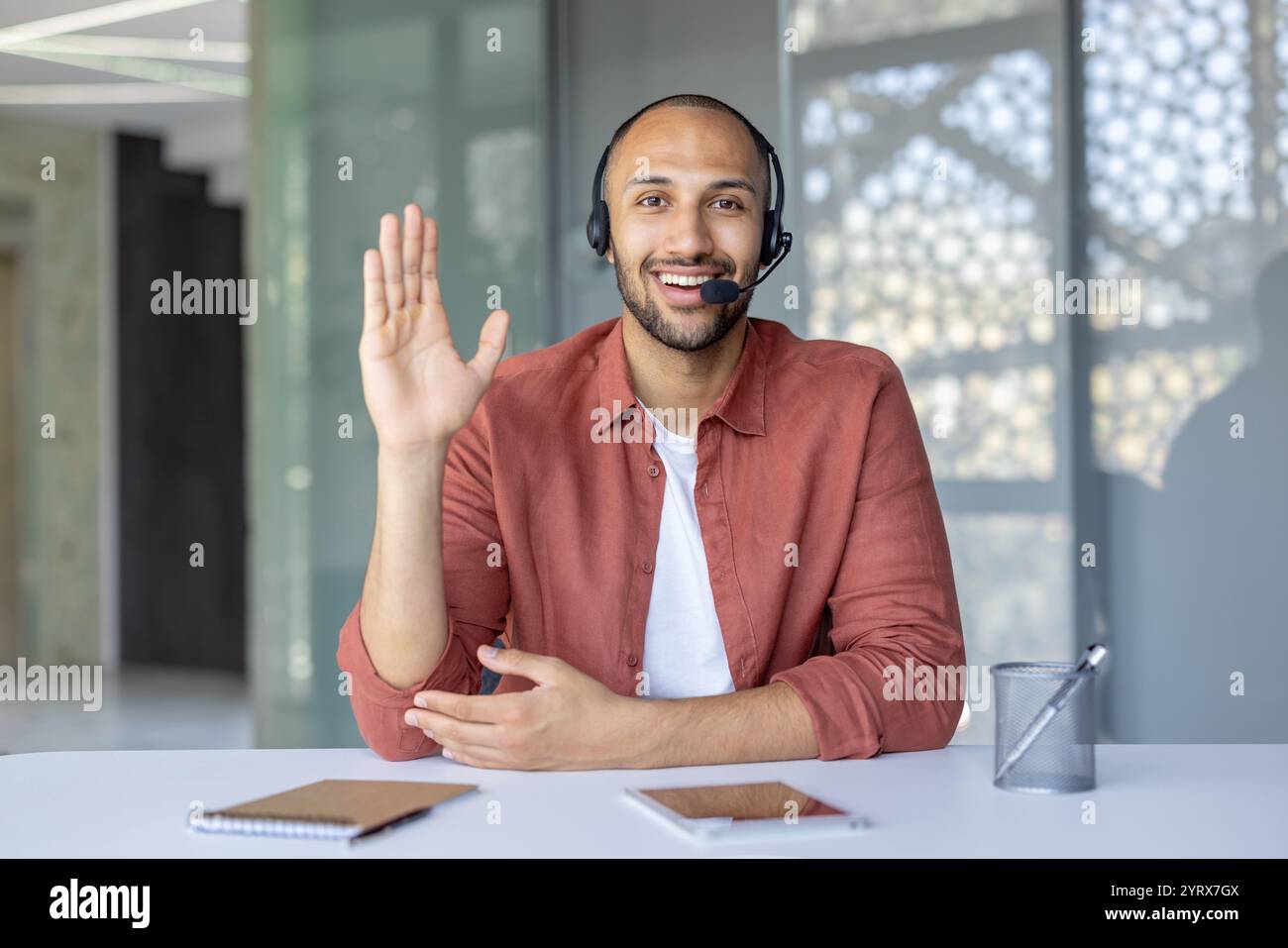 Ein selbstbewusster Geschäftsmann, der ein Headset trägt, nimmt an einem Online-Meeting Teil. Er sitzt am Schreibtisch mit Notizblock und Telefon und kommuniziert effektiv. Ideal für Unternehmens- und Kommunikationskonzepte. Stockfoto