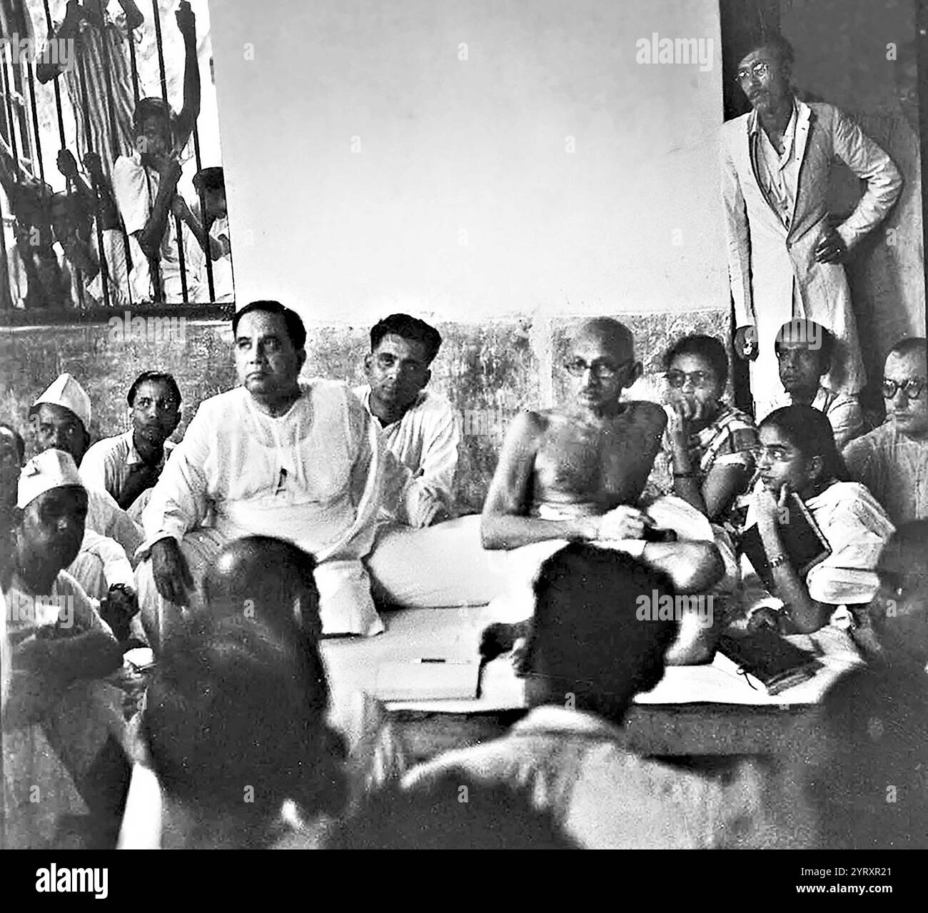 Mahatma Gandhi, der Vorsitzende des indischen Nationalkongresses, besuchte 1946 ein Haus in Noakhali in Begleitung des bengalischen Ministerpräsidenten Huseyn Shaheed Suhrawardy (rechts von Gandhi) und des jungen Aktivisten der All India Muslim League Sheikh Mujibur Rahman (stehend). Mahatma Gandhi wurde 1947 der Gründungsvater Indiens. H S Suhrawardy wurde 1957 Premierminister Pakistans. Scheich Mujibur Rahman wurde 1971 Gründungsvater und erster Präsident von Bangladesch. Stockfoto