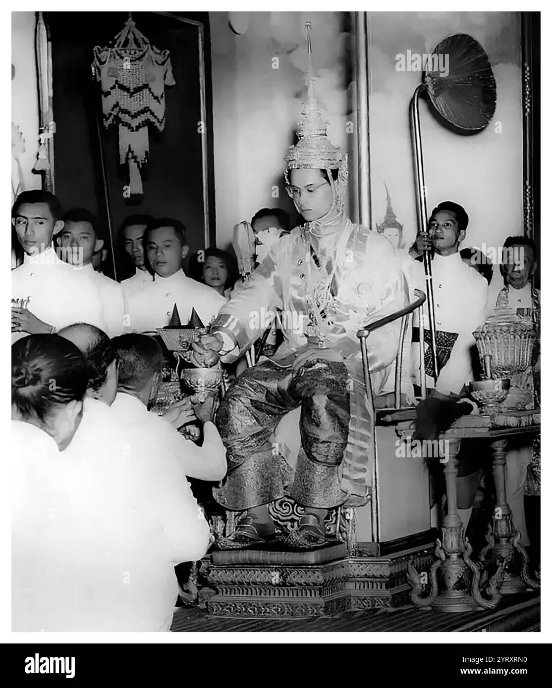 Krönung von Ananda Mahidol (20. September 1925? 9. Juni 1946) König von Siam (später Thailand) aus der Chakri-Dynastie mit dem Titel Rama VIII. Als er im März 1935 von der Nationalversammlung als König anerkannt wurde, war er ein neunjähriger Junge, der in der Schweiz lebte. Im Dezember 1945 kehrte er nach Thailand zurück, aber sechs Monate später, im Juni 1946, wurde er erschossen in seinem Bett aufgefunden. Sein Tod wurde von Gerichtsmedizinern als Mord eingestuft, und drei königliche Helfer wurden später nach sehr unregelmäßigen Gerichtsverfahren hingerichtet. Neben ihm (rechts) ist V Stockfoto