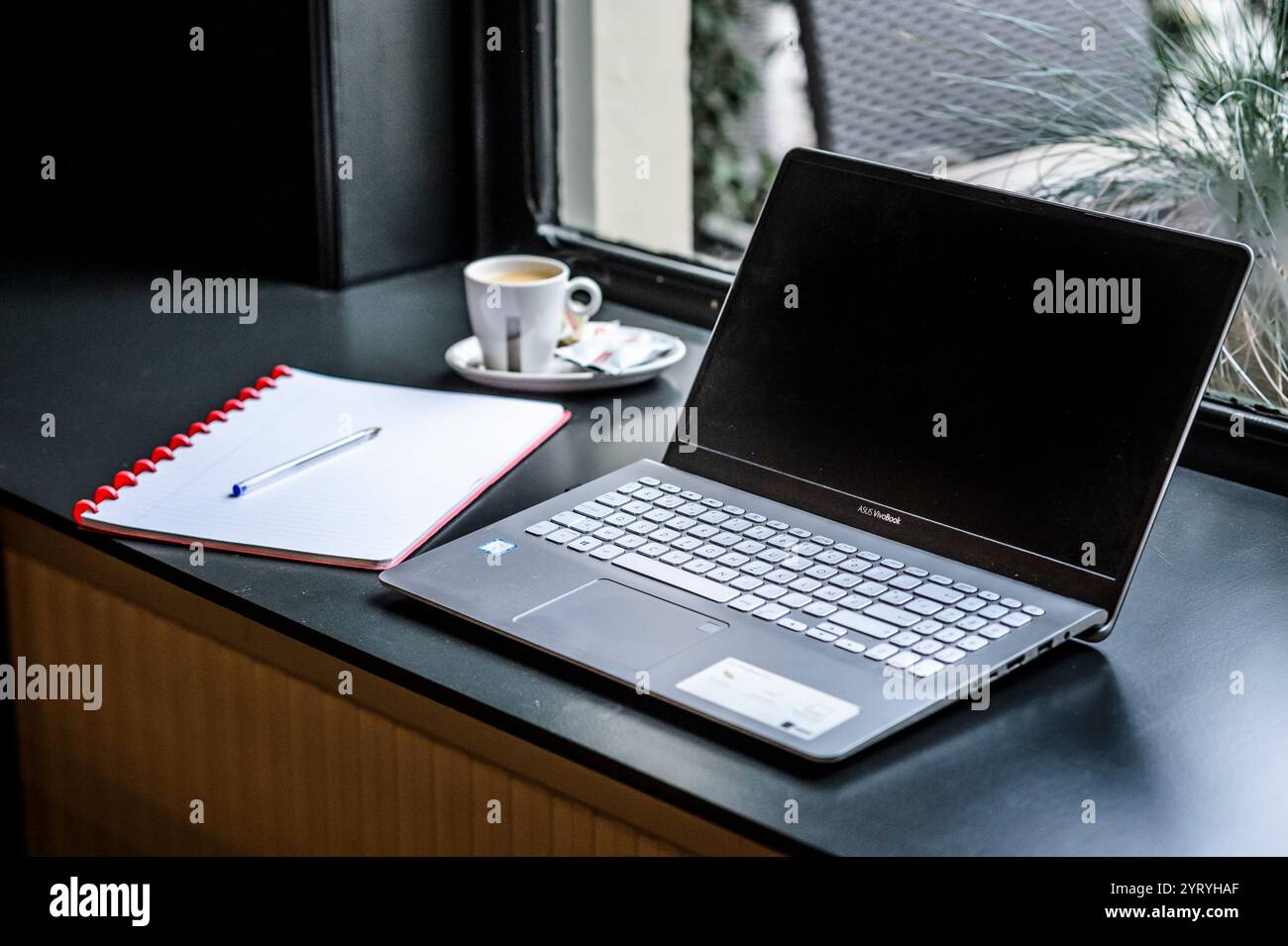 Laptop, Notebook und Espresso an einem modernen Arbeitsplatz am Fenster, ideal für Fernarbeit, Studium oder kreative Projekte. Stockfoto
